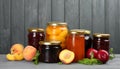 Glass jars with different pickled fruits and jams on wooden background