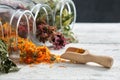 Glass jars of dry medicinal herbs - raspberry leaves, calendula, coneflowers and linden tree flowers on table.