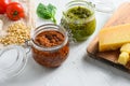 Glass jars with red and green pesto and cooking ingredients Parmesan cheese, basil leaves, pine nuts, white stone background, Royalty Free Stock Photo