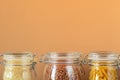 Glass jars with uncooked cereals, pasta, rice, buckwheat on a beige background. Zero waste concept, housewares