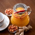 Glass jug of sea buckthorn ginger tea with chili pepper. Hot vitamin drink on wooden table, top view. Healthy lifestyle Royalty Free Stock Photo