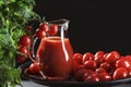 Glass jug with tomato juice stands covered with cherry tomatoes next to a natural tomato bush, conceptual image Royalty Free Stock Photo