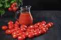 Glass jug with tomato juice stands covered with cherry tomatoes next to a natural tomato bush, conceptual image Royalty Free Stock Photo
