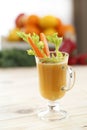 A glass of juice in a glass latte mugs with a pieces of celery and carrots with a colored background