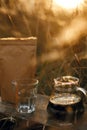 Glass kettle with coffee, cup and brown pack with coffee on background of rural countryside herbs in sunset. Alternative coffee