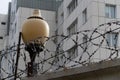 Glass lantern on a fence with barbed wire, against the background of a tall building Royalty Free Stock Photo