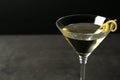 Glass of lemon drop martini cocktail with zest on stone table against black background, closeup.