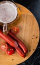 Glass of light beer, meat sausages and tomatoes on wooden board Royalty Free Stock Photo