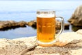 Glass of light beer near sea. Misted mug, pint of cold beer stands against background of blurred sea landscape in cafe, restaurant Royalty Free Stock Photo