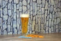 A glass of light beer with white foam on a white and blue napkin and several pretzels with salt on a wooden table