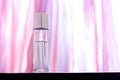 A glass long bottle with perfume stands on a bright pink background with overexposure.