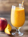 Glass of mango peach smoothie with mango chunks, peach slices, and ice cubes, garnished with a peach slice on the rim Royalty Free Stock Photo