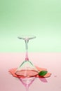 Glass martini glass and spilled liquid on a pink-green background. Modern art photography Royalty Free Stock Photo