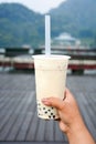 Glass of milk bubble tea with tapioca pearls in tourist hand with sun moon lake background, Taiwan