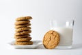 A glass of milk with a ginger cookie leaning against it next to a stack of ginger cookies on a white plate with a white background Royalty Free Stock Photo