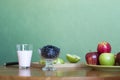 A glass of milk, a plate of apples, a bowl of blueberries on a green background Royalty Free Stock Photo