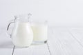 Glass of milk with small jug of milk on white wooden table Royalty Free Stock Photo