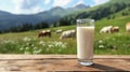 A glass of milk stands on a wooden table. Behind is a blurred background of an alpine meadow on which cows graze Royalty Free Stock Photo