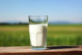 Glass of milk on wooden table with lush green field and clear blue sky. Copy space