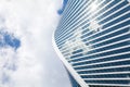 Glass mirror skyscraper wall spiral shape on blue sky, white clouds background, modern business center building