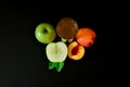 A glass of a mixture of fruit juices and slices of ripe peach and green apple on a black background
