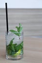 Glass of mochito cocktail on wooden table with black straw, ice and mint leaf