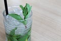 Glass of mochito cocktail on wooden table with black straw, ice and mint leaf