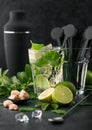 Glass of Mojito cocktail with ice cubes and disk stirrers,mint and lime on black board with spoon and fresh limes with cane sugar Royalty Free Stock Photo