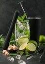 Glass of Mojito cocktail with ice cubes mint and lime on black board with spoon in shake and black muddler and fresh limes with Royalty Free Stock Photo