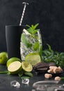 Glass of Mojito cocktail with ice cubes mint and lime on black board with spoon in shake and wooden squeezer and fresh limes Royalty Free Stock Photo