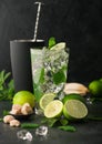 Glass of Mojito cocktail with ice cubes mint and lime on black board with spoon in shaker and wooden squeezer and fresh limes Royalty Free Stock Photo