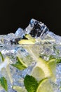 Glass of Mojito summer alcoholic cocktail with ice cubes mint and lime on black background with raw lime and mint leaf Royalty Free Stock Photo