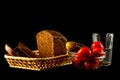 The glass of moonshine,salted cucumber with tomatoes in glass vase and loaf of fresh rye bread with slices isolated on a black.