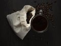 Glass mug with fresh black natural coffee, a bag with coffee grains and sprinkled grains of roasted coffee on a wooden table Royalty Free Stock Photo