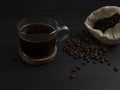 Glass mug with fresh black natural coffee, a bag with coffee grains and sprinkled grains of roasted coffee on a wooden table Royalty Free Stock Photo