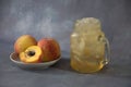 Glass mug of fruit juice with ice and a plate with cutted and whole peaches on a gray background