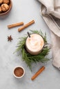 Glass mug of hot chocolate with whipped cream on a stand with pine branches on a light background with cinnamon stick , cookies,