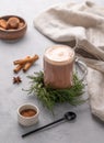 Glass mug of hot chocolate with whipped cream on a stand with pine branches on a light background with cinnamon stick , cookies,