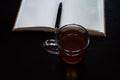 A glass mug with tea and a lemon slice, notebook with blank pages, black pen on dark desk Royalty Free Stock Photo