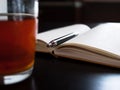 A glass mug with tea and a lemon slice, notebook with blank pages, black pen on dark desk Royalty Free Stock Photo