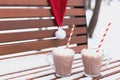 Glass mugs, cups with hot chocolate, cocoa, marshmallows. Santa Claus hat. Winter snow covered park bench. Striped red paper Royalty Free Stock Photo