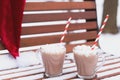 Glass mugs, cups with hot chocolate, cocoa, marshmallows. Santa Claus hat. Winter snow covered park bench. Striped red paper Royalty Free Stock Photo