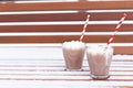 Glass mugs, cups with hot chocolate, cocoa, marshmallows. Winter snow covered park bench. Striped red, white paper straws for Royalty Free Stock Photo