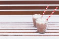 Glass mugs, cups with hot chocolate, cocoa, marshmallows. Winter snow covered park bench. Striped red, white paper straws for Royalty Free Stock Photo