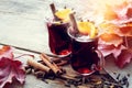 Glass mugs of mulled wine on wooden table with fallen maple leaves.