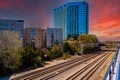 Glass office buildings and apartments along side a set of railroad tracks surrounded by lush green trees with  powerful red clouds Royalty Free Stock Photo