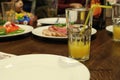 A glass of orange apricot yellow juice in a glass with a straw stands near a plate in the cafe`s restran. Lunch at the cafe Royalty Free Stock Photo