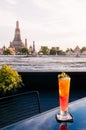 Glass of orange cocktail with orange slices on bluish black table with Wat Arun pagoda and Chao Praya river view, Bangkok Royalty Free Stock Photo