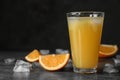 Glass of orange juice with ice cubes and cut fruit on table against black background Royalty Free Stock Photo