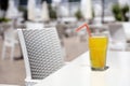 Glass of orange juice with plastic straw on white table in restaurant outdoor lounge zone Royalty Free Stock Photo